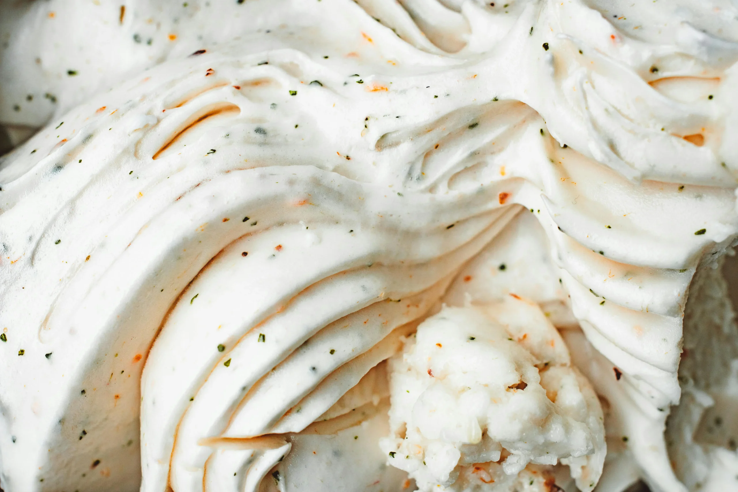 Close-up of a whipped cream swirl with specks of vanilla bean and orange zest, suggesting a rich and flavorful dessert topping.