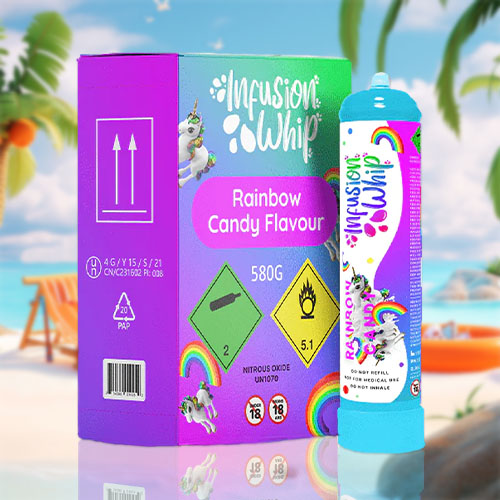 The image features a colorful "InfusionWhip" product set against a beach scene. On the left, a purple box is adorned with unicorn graphics and displays a green label that reads "Rainbow Candy Flavour," indicating the flavor of the cream chargers it contains. The box has safety markings, such as nitrous oxide content and standard hazard symbols, including flammability and age restriction warnings. On the right is a matching canister, turquoise with playful decorations, including a rainbow, sparkles, and a unicorn, similar to the box's theme. It's labeled with a net content of "580g" and has safety advisories such as "Do not refill," "Not for medical use," and "Do not inhale." This whimsical and vibrant packaging contrasts with the tranquil beach setting, which includes a clear blue sky, palm trees, and beach accessories, highlighting the product's fun and flavorful characteristics.